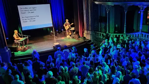 Musiker mit Publikum, auf Leinwand zu lesenden Text singend